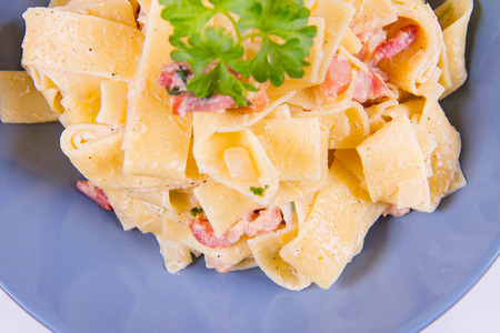 Pappardelle Carbonara with some parsley on a blue plate on a white backgroundの写真素材