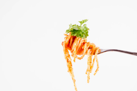 Spaghetti with pesto rosso on a fork with parsley on a white backgroundの写真素材