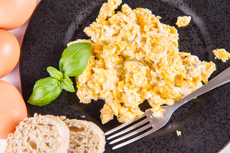 Scrambled eggs, wholemeal bread, and a fork, decorated with basil, on a white backgroundの写真素材