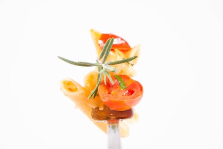Penne with tomatoes, garlic and mozzarella on a fork decorated with rosemary twig on a white backgroundの写真素材