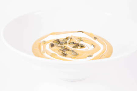 Pumpkin soup decorated with cream and pumpkin seeds on a plate on a white backgroundの写真素材