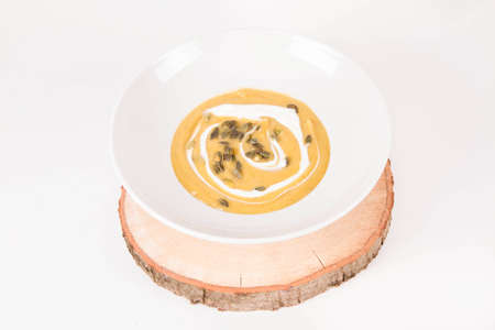 Pumpkin soup decorated with cream and pumpkin seeds on a plate on a piece of woodの写真素材