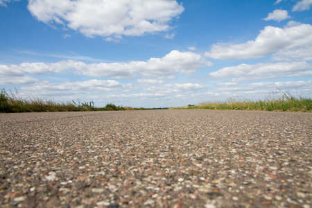 Road among fields in the summer, with blue sky and white clouds above