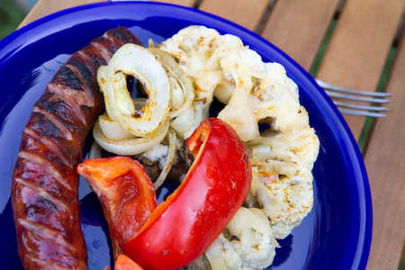 Barbequed sausages, red bell pepper, onion rings and cauliflower covered with melted cheeseの写真素材