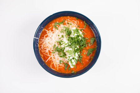 Italian tomato soup served with cream, mozzarella cheese and fresh parsley in a bowl, on a white backgoundの写真素材