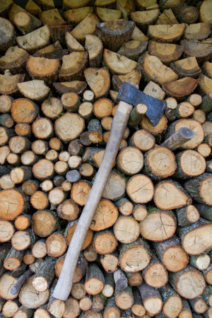 Woodpile of tree trunks, waiting to be chopped for firewood, with an ax mounted on it