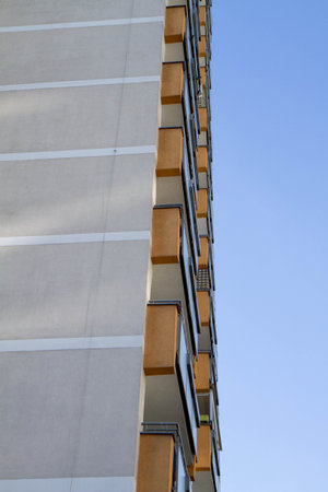 Facade of modern apartment building with rows of balconies visible. Close up with blue sky in the...