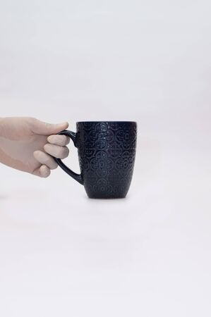 A hand wearing a white glove holding a handle of a blue coffee mug in order to protect from virusの写真素材