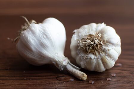 Two white garlic placed on a wooden floor with few droplets on themの写真素材