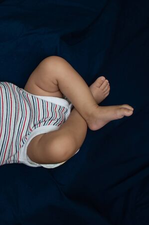 Small baby's folded legs on a blue bed sheet
