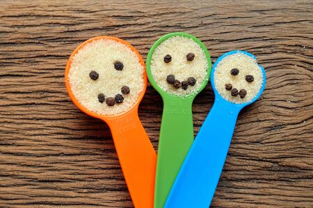 Happy family faces of  plastic measuring spoons on wood with  sugar and pepper seedsの写真素材