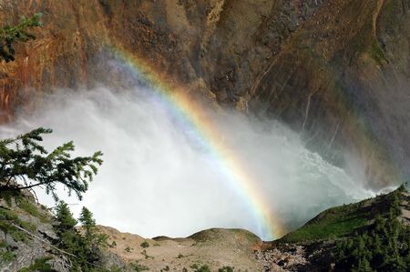 A view at the base of a water fall where a rainbow forms in it's mist.の写真素材