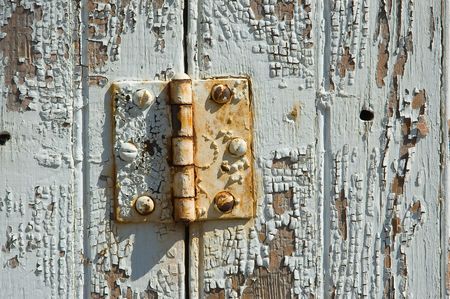An old rusty door hinge mounted on a paint-flaking door.の写真素材