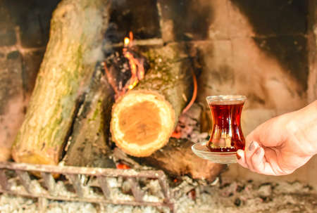 Closeup of cup with famous traditional Turkish tea in front cozy and worm fireplace, in country house. Winter or autumn (fall) vacation in Turkey.の写真素材