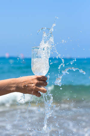 Glass of fresh clear cold water with ice and blue ocean on the background. Healthy lifestyle. Glass...