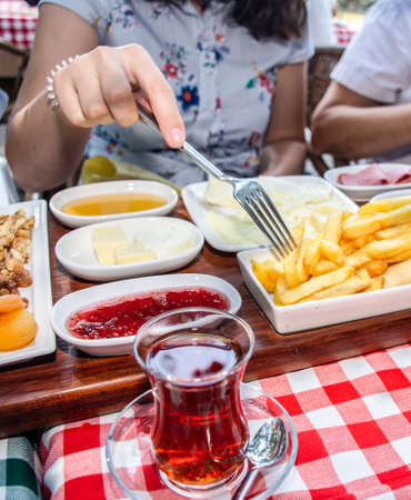 Family having delicious rich traditional Turkish breakfast include tomatoes, cucumbers, cheese, butter, eggs, honey, bread, olives, jam, sausage, fried potatoes and tea cups.の写真素材