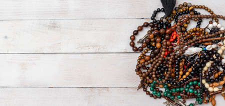 Many kind of Rosaries in different colors and sizes on white wooden background. Multicolored beads...