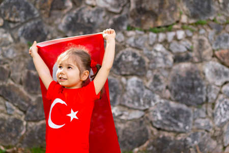Little girl in a red dress holds a flag of Turkey in her hands.