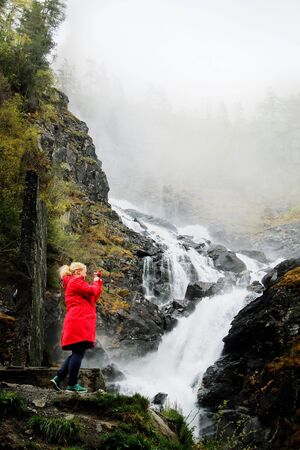 Girl photographing waterfall with a mobile phoneの素材