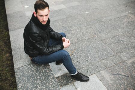 A man dressed in jeans and black jacket seats on a slabの写真素材