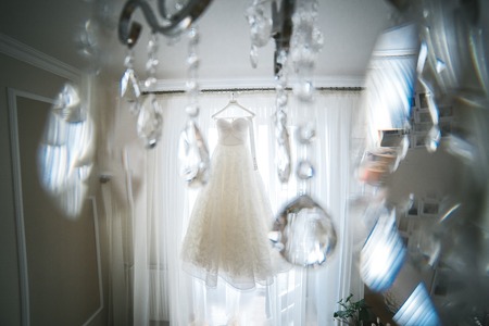 a beautiful white wedding dress hanging in the background of a large windowの写真素材