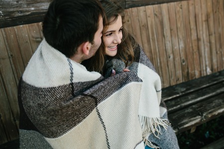 Young couple in love wrapped in plaid sitting and having funの写真素材