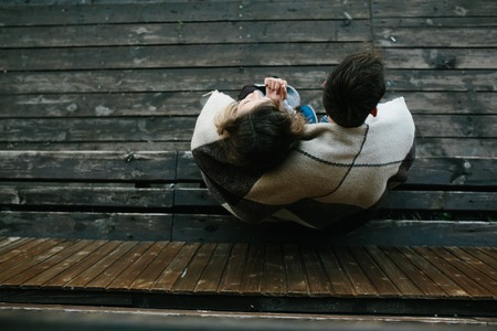Young couple in love wrapped in plaid sitting and having funの写真素材