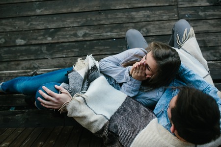 Young couple in love wrapped in plaid sitting and having funの写真素材