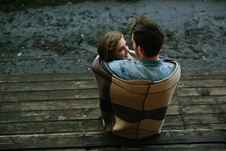 Young couple in love wrapped in plaid standing and looking at each otherの写真素材