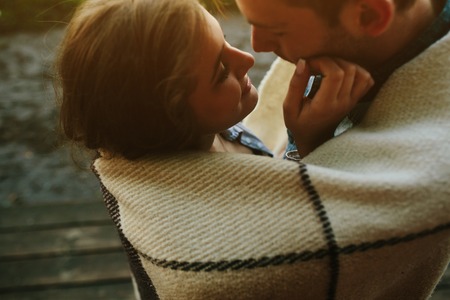 Young couple in love wrapped in plaid standing and looking at each otherの写真素材