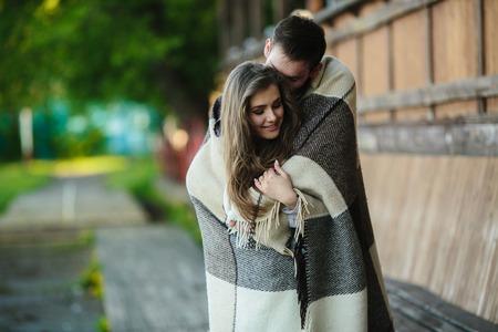 Young couple in love wrapped in plaid standing and looking at each otherの写真素材