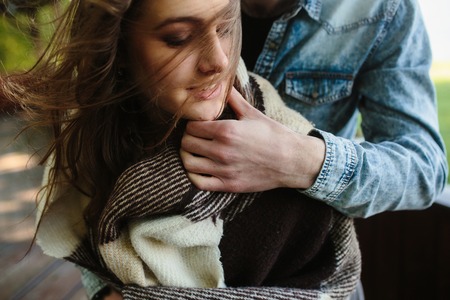 Young couple in love wrapped in plaid standing and embraceの写真素材