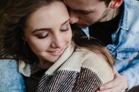 Young couple in love wrapped in plaid standing and embraceの写真素材