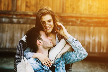 Young couple in love wrapped in plaid standing and embraceの写真素材