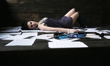girl posing in a dark room on the floor among the sheets of paperの写真素材