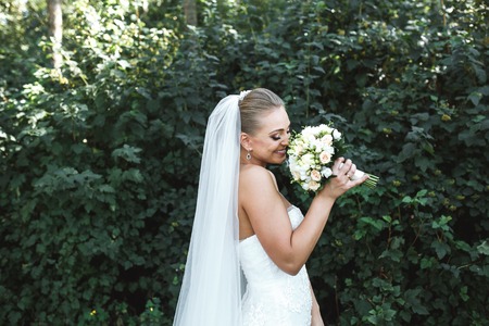 Beautiful bride posing in the park on the background of foliageの写真素材