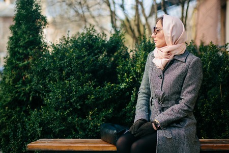 young beautiful happy girl in a coat sitting on a bench in the parkの写真素材