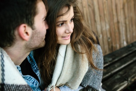 Young couple in love wrapped in plaid sitting and having funの写真素材