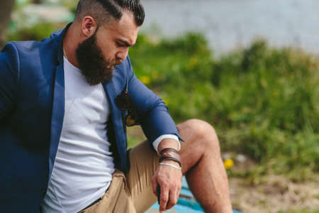 American Bearded Man looks on the river bank in a blue jacket