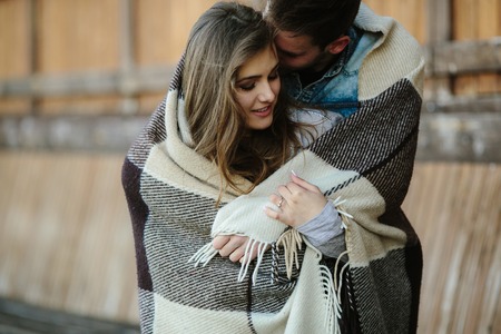 Young couple in love wrapped in plaid standing and looking at each otherの写真素材
