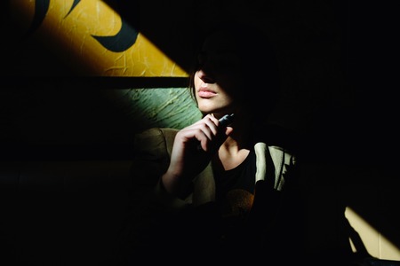 mysterious young girl sits and smokes electronic cigaretteの写真素材