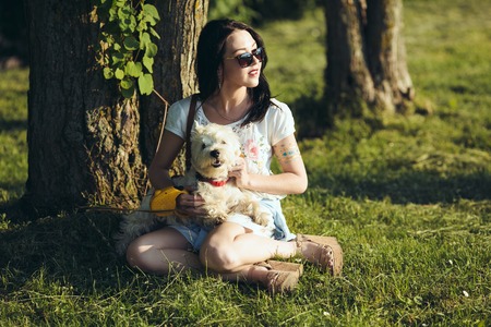 The girl with a dog sit on a grass under the treeの写真素材
