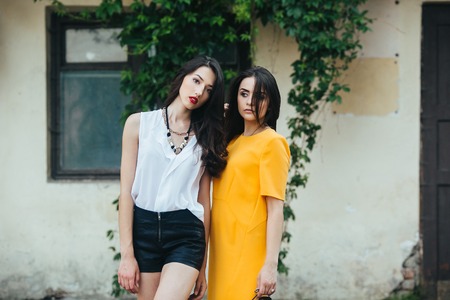 Two beautiful young girls in dresses posing in front of houseの写真素材