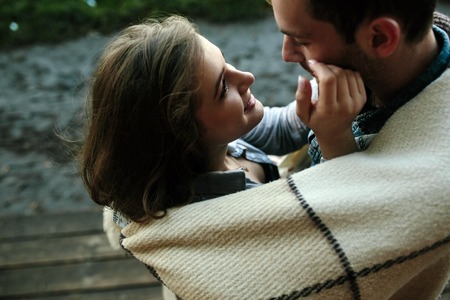 Young couple in love wrapped in plaid standing and looking at each otherの写真素材