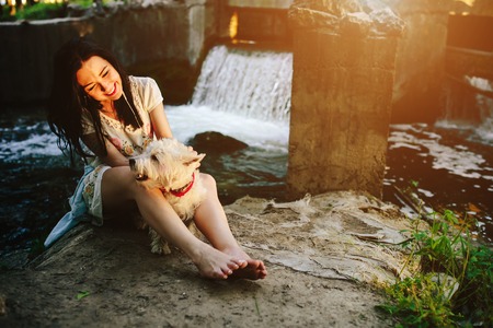 girl playing with a dog on the bank of the river near the bridgeの写真素材