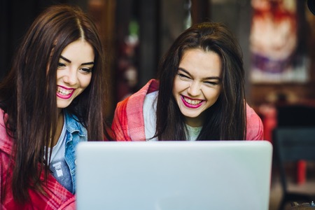 Two young and beautiful girl sitting at the table and looking for something on the Internetの写真素材