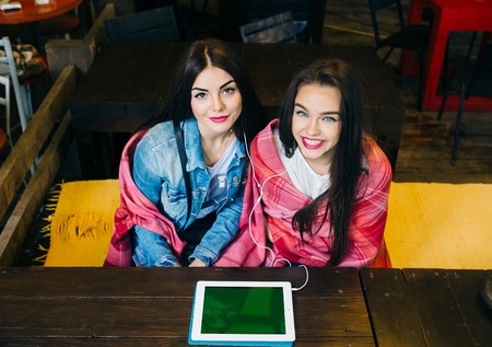 Two young and beautiful girl sitting at the table watching something on a tablet