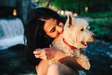 girl playing with a dog on the bank of the river near the bridgeの写真素材