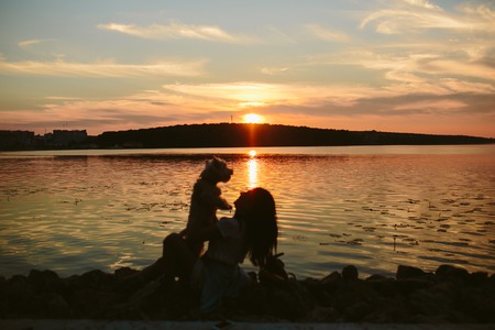 Girl and dog on the lake on sunset backgroundの写真素材