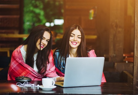 Two young and beautiful girl sitting at the table and looking for something on the Internetの写真素材